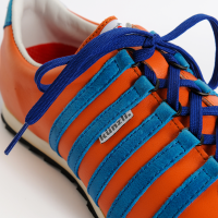 Sneaker Courage ist ein ausdrucksvoller Eyecatcher. Der orange Schuh aus Leder mit blauen K&#252;nzli-Streifen und coolem Charakter. Edelsneaker
